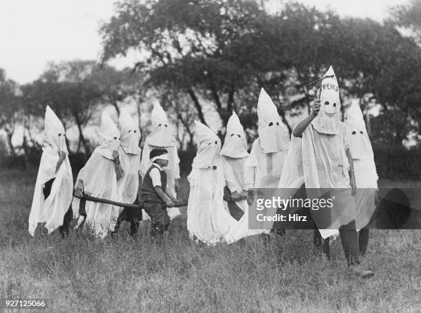 Blindfolded candidate is carried to a secret meeting place by a group of children mimicking the regalia and activities of the Ku Klux Klan, East...
