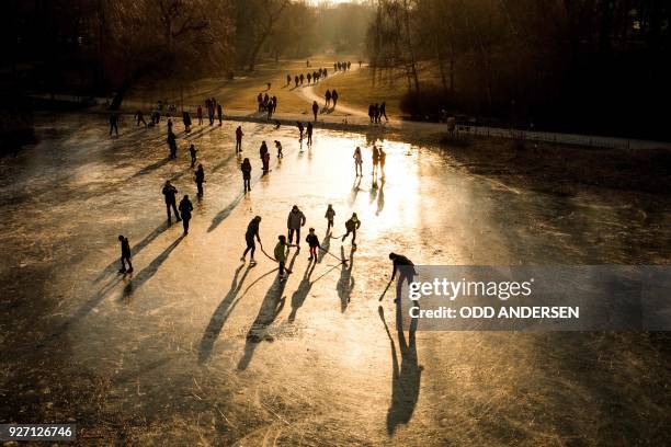 The sun sets as people play on a frozen pond and walk along the paths of a park next to Schoeneberg town hall in Berlin on March 4, 2018.