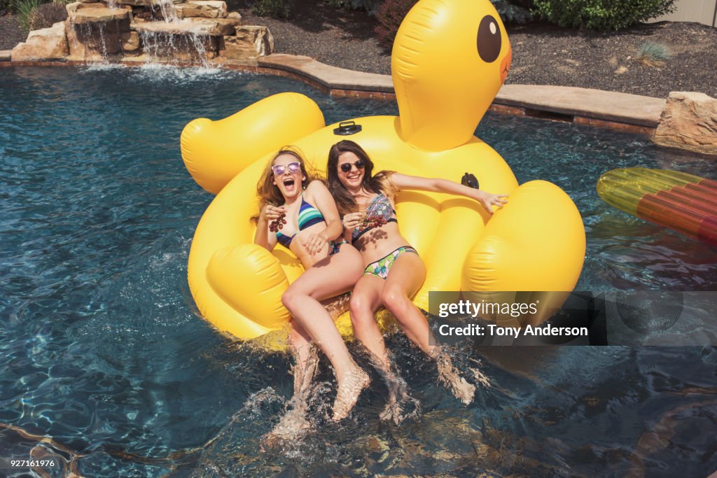 Two teenaged girls on rubber duck raft in swimming pool
