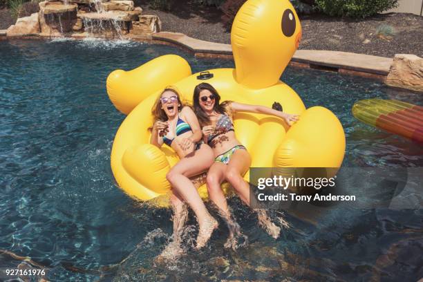 two teenaged girls on rubber duck raft in swimming pool - girls sunbathing fotografías e imágenes de stock