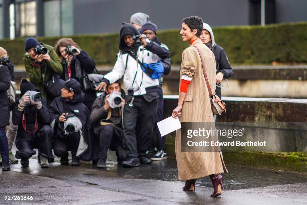 Yasmin Sewell wears a trench coat, an orange turtleneck, a polka dots skirt, boots, outside Valentino, during Paris Fashion Week Womenswear...