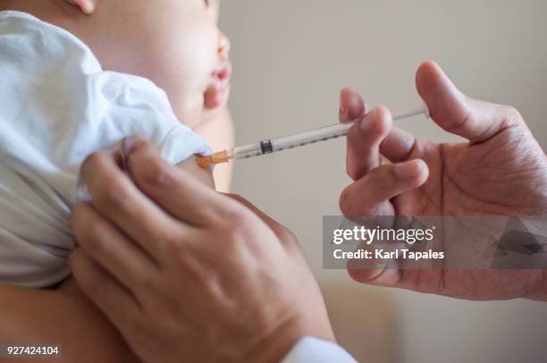 a doctor is injecting a vaccine to a baby boy - vacuna fotografías e imágenes de stock