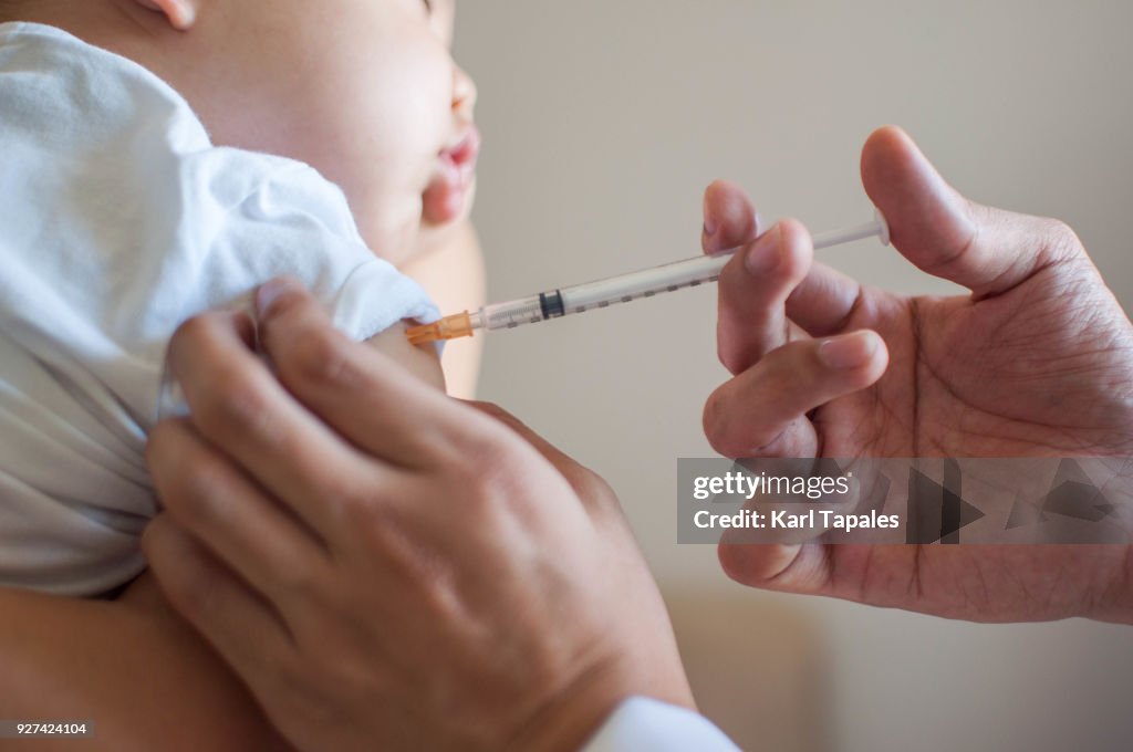 A doctor is injecting a vaccine to a baby boy