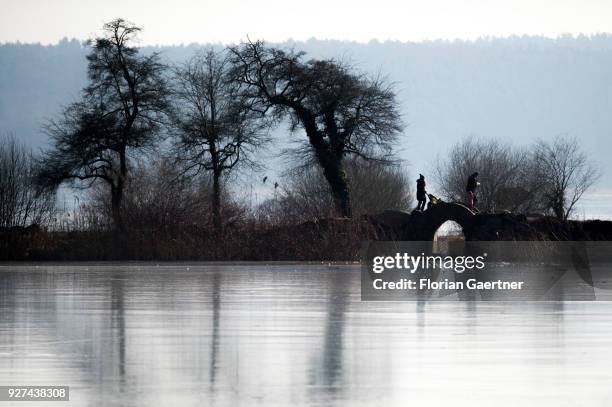 Woman with a buggy and a man with a child walk over a little bridge at a frozen lake near the lake Schwielowsee on March 03, 2018 in Petzow, Germany.