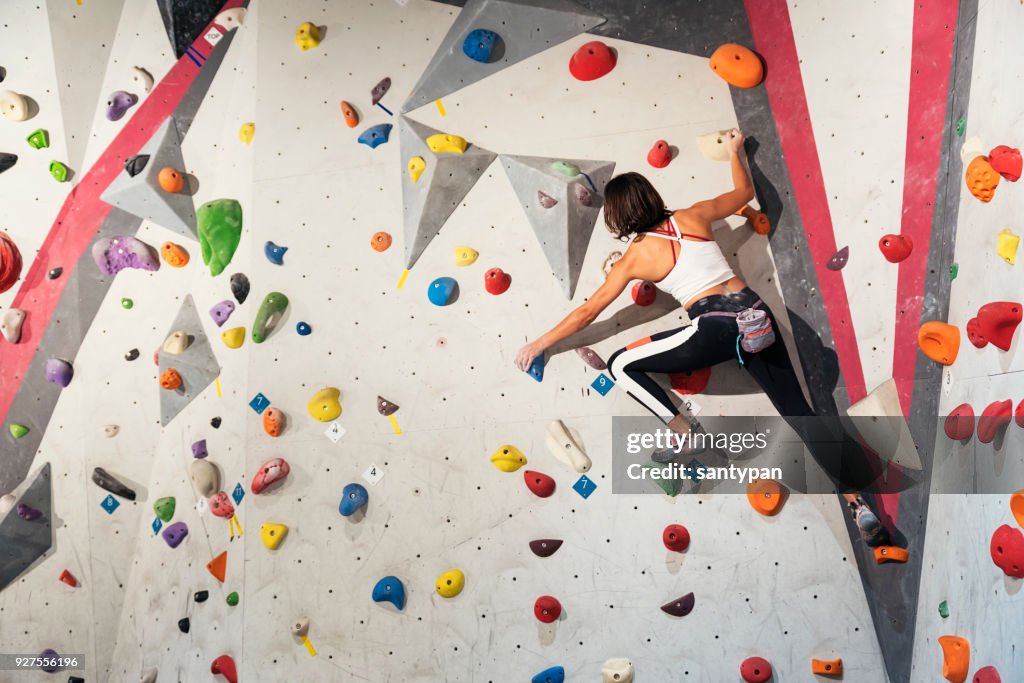 Woman practicing rock climbing on artificial wall indoors. Active lifestyle and bouldering concept.