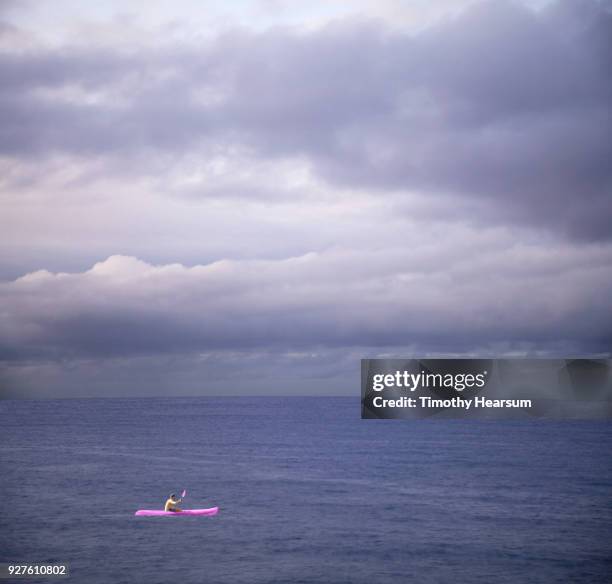 kayaker in bright ultraviolet vessel paddling in an ultraviolet sea with ultraviolet clouds beyond - timothy hearsum stock pictures, royalty-free photos & images