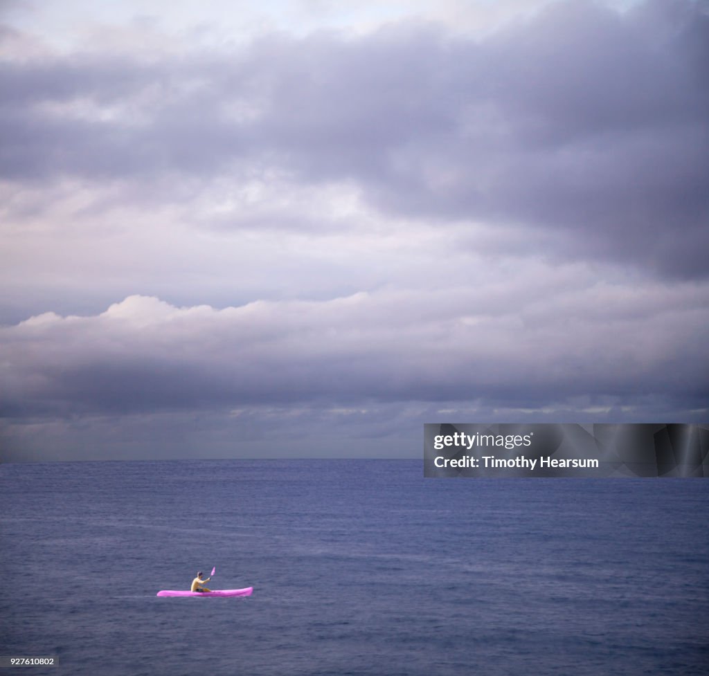 Kayaker in bright ultraviolet vessel paddling in an ultraviolet sea with ultraviolet clouds beyond