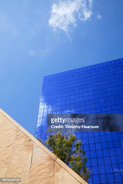 detail view of city skyscraper with cloud reflections against a mostly blue sky; neutral wall in foreground - timothy hearsum stock-fotos und bilder