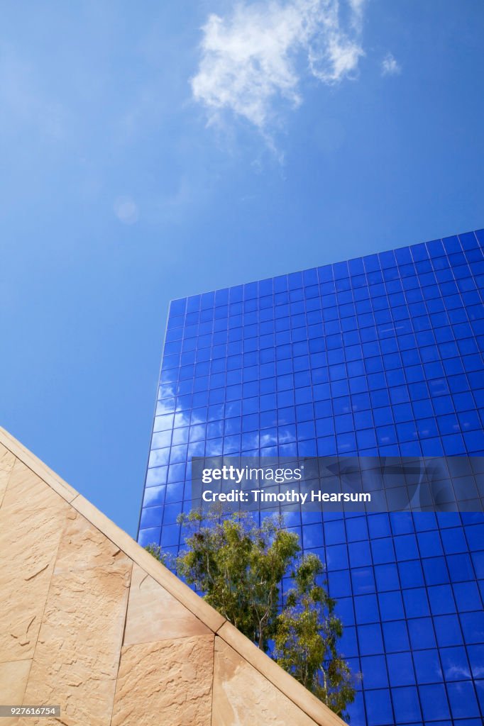 Detail view of city skyscraper with cloud reflections against a mostly blue sky; neutral wall in foreground