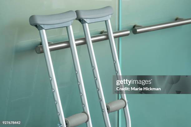 pair of metal crutches leaning against a modern steel handle on a glass door. - accident recovery stockfoto's en -beelden