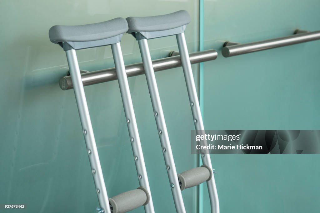 Pair of metal crutches leaning against a modern steel handle on a glass door.