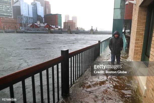 Man walks slowly through a flooded sidewalk off Congress Street in Boston, where water was flowing over from Fort Point Channel in the Seaport...