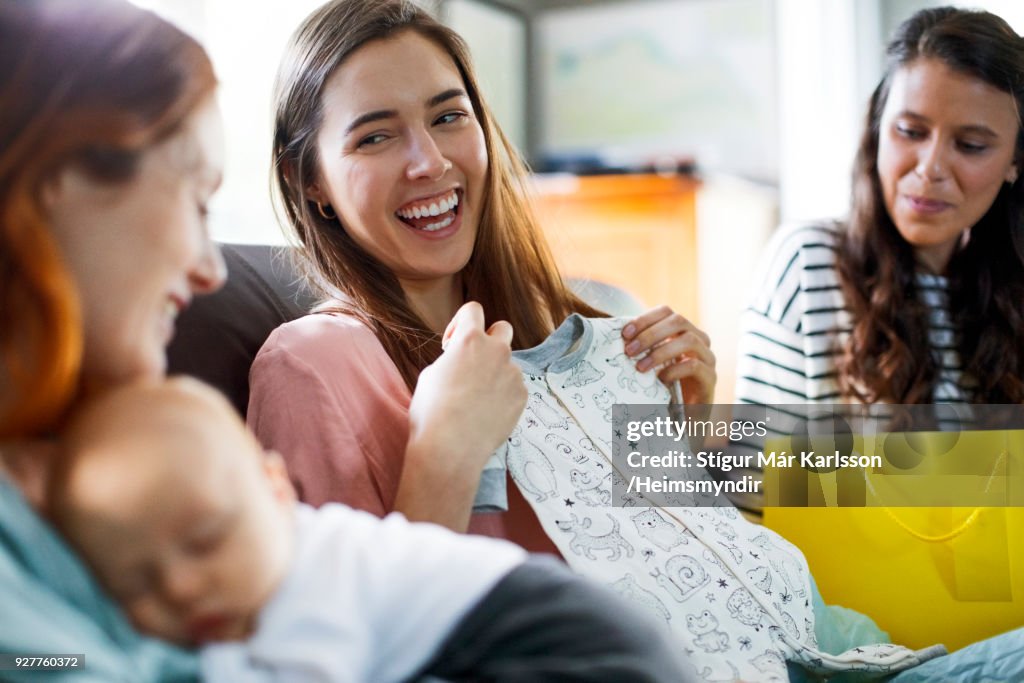 Happy pregnant woman with baby clothing by friends