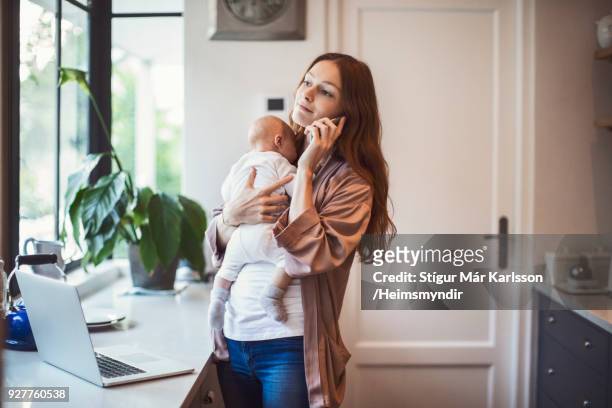 moeder met behulp van de telefoon terwijl de uitvoering van de baby in de keuken - busy woman stockfoto's en -beelden