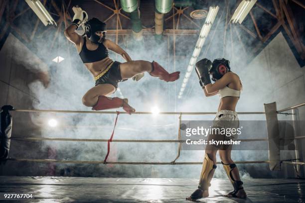 sportliche frau macht eine fliegende bewegung auf ein kickbox-match mit ihrer gegnerin. - free fight stock-fotos und bilder