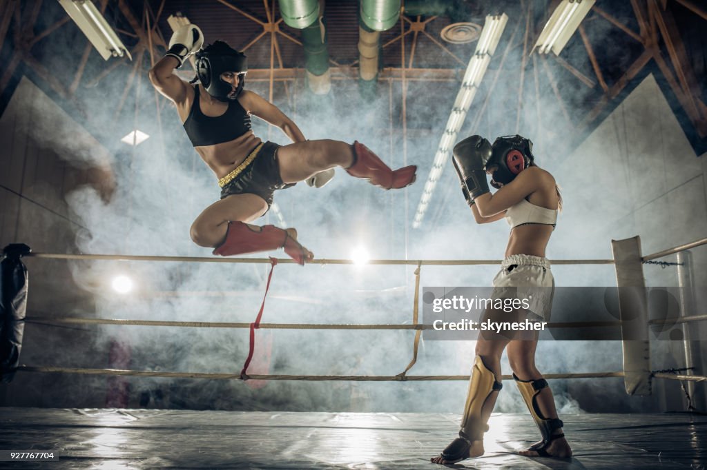 Mujer atlética hacer un movimiento vuelo en un combate de kickboxing con su oponente.