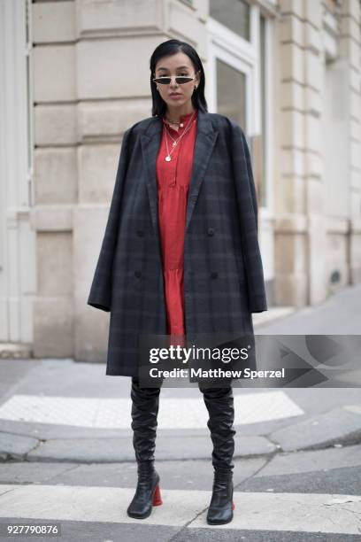 Guest is seen on the street attending A.P.C. During Paris Women's Fashion Week A/W 2018 wearing a navy coat with red dress and black thigh-high boots...