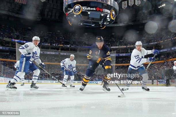 Zemgus Girgensons of the Buffalo Sabres skates with the puck against Jake Gardiner and Nikita Zaitsev of the Toronto Maple Leafs during an NHL game...