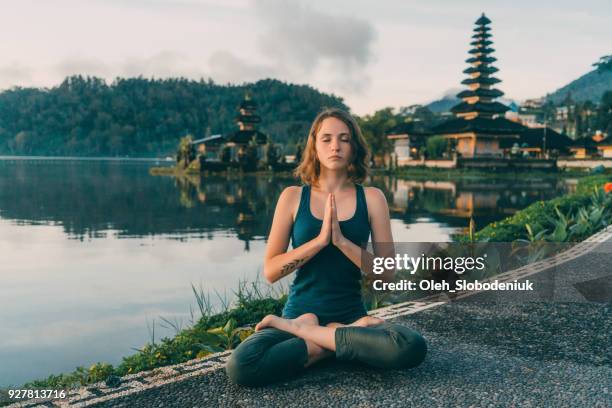 woman doing yoga near ulun danu temple in bali at sunrise - lotus position stock pictures, royalty-free photos & images