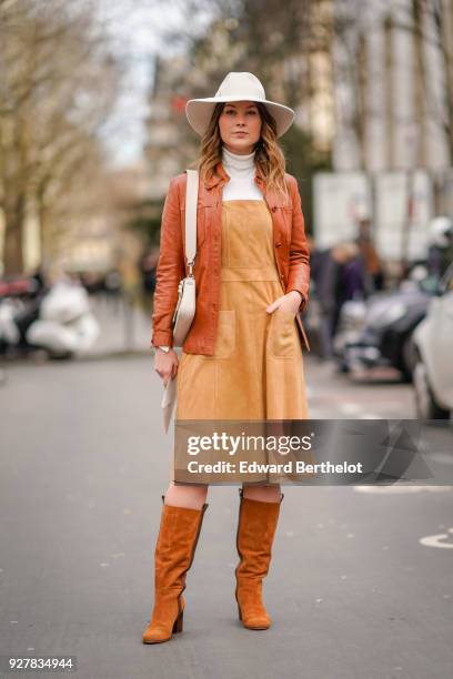 Angelica Ardasheva wears a white hat, a brown leather jacket, orange dress, brown leather boots, outside Giambattista Valli, during Paris Fashion...