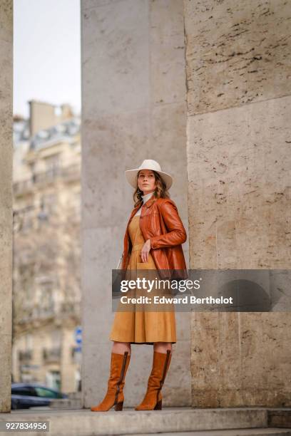 Angelica Ardasheva wears a white hat, a brown leather jacket, orange dress, brown leather boots, outside Giambattista Valli, during Paris Fashion...