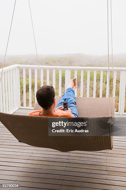 man using a mobile phone on a porch swing - hollywoodschaukel stock-fotos und bilder