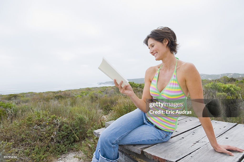 Woman sitting on a boardwalk and reading a book