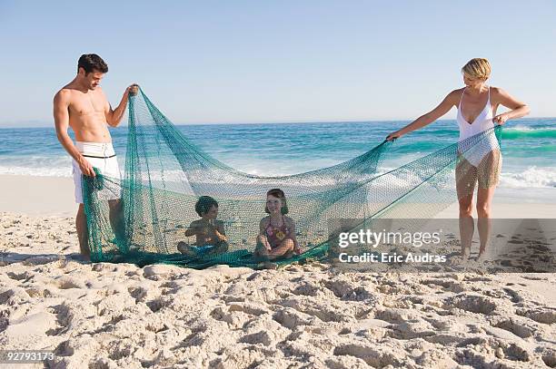 family playing with a fishing net on the beach - flirt barefoot blonde stock-fotos und bilder