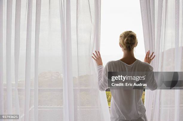 rear view of a woman opening the curtain of balcony - see thru nightgown photos et images de collection