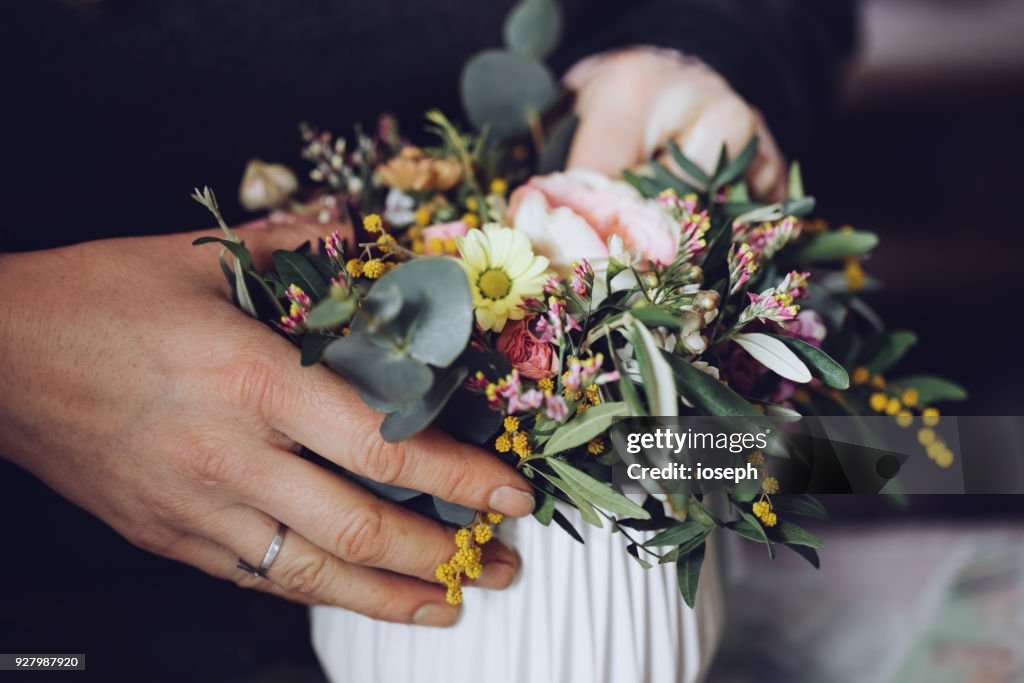Modern florist working with flowers in workshop - with detail on hands