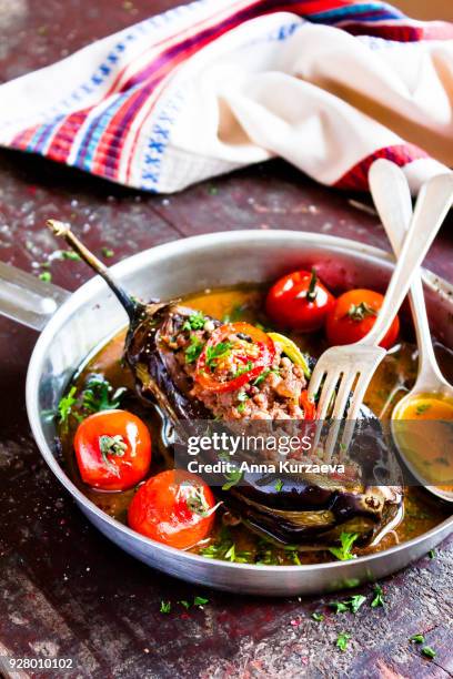 baked aubergine or eggplant stuffed with minced pork and beef, carrot, pepper, cherry tomatoes in a pan on a wooden table, selective focus - griekse gerechten stockfoto's en -beelden