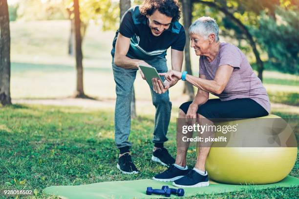 fitness instructor and senior woman with digital tablet - wellness program stock pictures, royalty-free photos & images