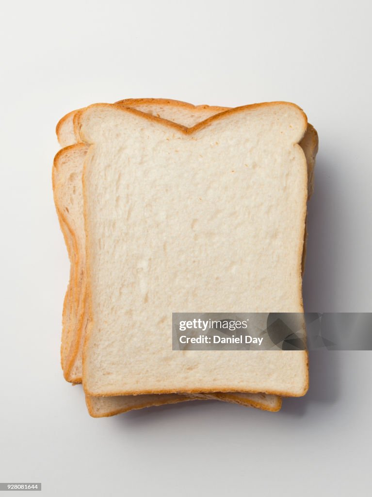 Series of different sliced white bread slices, some with butter, crust and pile of slices against a white background shot from above