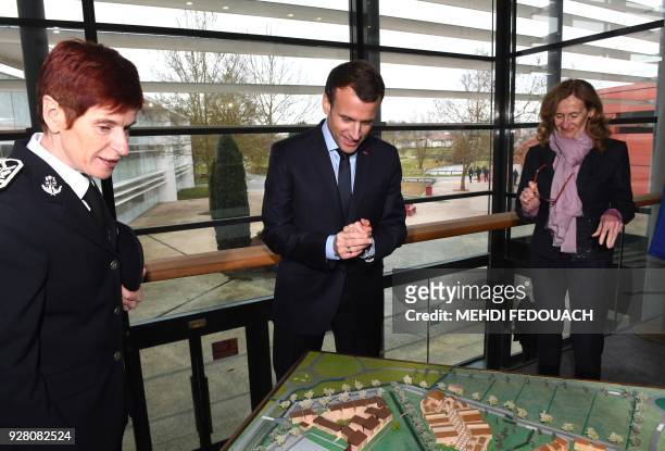 French president Emmanuel Macron flanked by prison guard school director Sophie Bleuet and French Justice Minister Nicole Belloubet look at a scale...