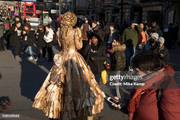 Girls try to distract a gold living statue street performer in Piccadilly Circus in London, England, United Kingdom.