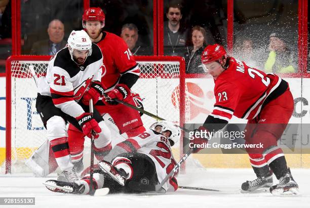 Brock McGinn of the Carolina Hurricanes looks to gain control of a loose puck near the crease as Damon Severson of the New Jersey Devils gos down...