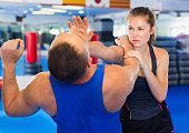 Woman is training with man on the self-defense course in gym.