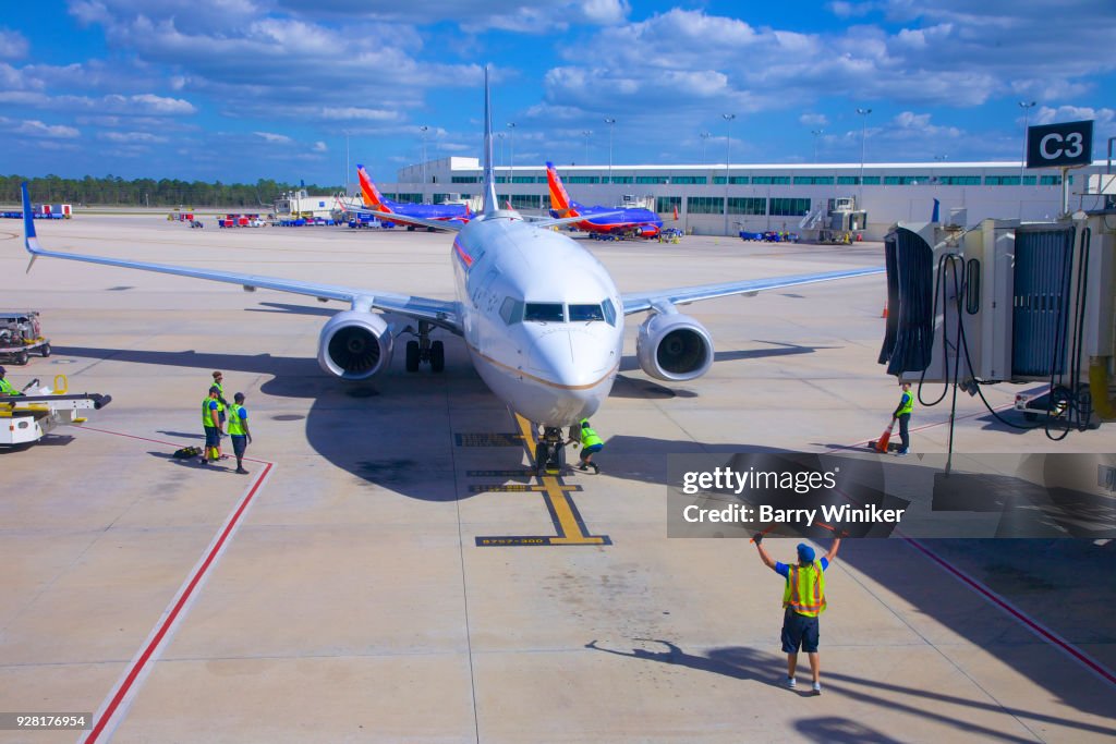 Workers guiding pilot in plane to parking position on tarmac
