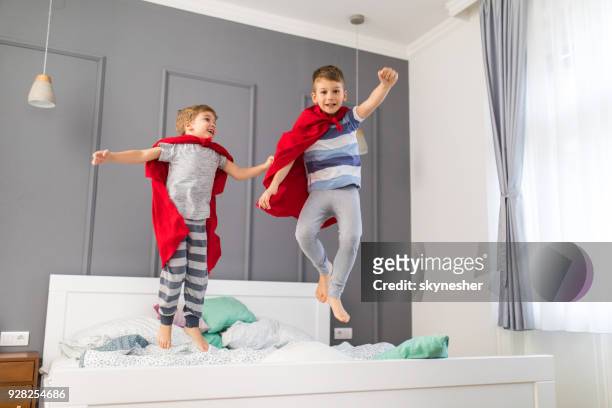 two playful boys having fun while jumping on a bed and pretending to be superheroes. - a boy jumping on a bed stock pictures, royalty-free photos & images