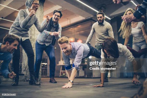 large group of happy freelancers having fun while having wheelbarrow race at casual office. - businesswoman handstand stock pictures, royalty-free photos & images