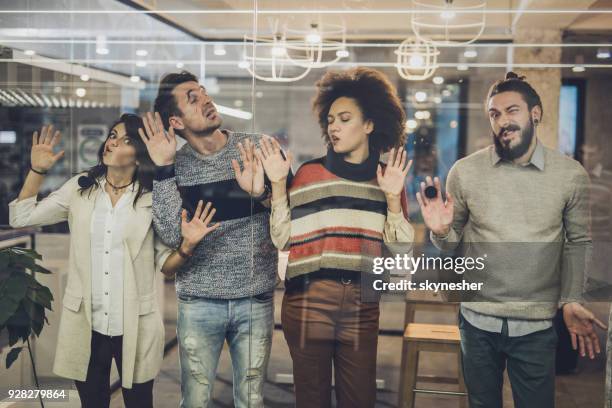 playful colleagues having fun while sticking their faces on glass wall. - sticky stock pictures, royalty-free photos & images