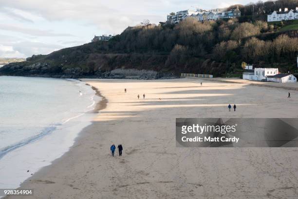 People walk on the beach at Carbis Bay near St Ives on March 6, 2018 in Cornwall, England. Last week freezing weather conditions dubbed the 'Beast...