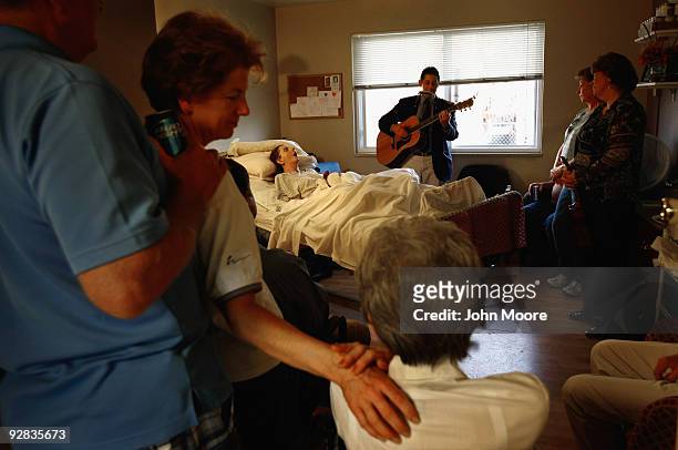 Family members gather around the bed of terminally ill hospice patient Linda Fletcher as musician Bob Haworth plays for her at the Hospice of Saint...