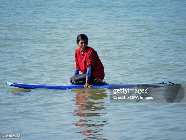 Young surfer seen taking a rest on her surfing board. Young people in the world´s longest sandy beach in Cox´s Bazar, Bangladesh, decided to throw...