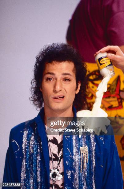 Portrait of Canadian actor and comedian Howie Mandel as he makes a face, Los Angeles, California, 1985. Beside him, a hand upends a prop jar of...