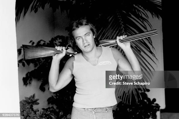 Portrait of British musician and lyricist Bernie Taupin as he poses with a shotgun over his shoulders, Los Angeles, California, April 1980.