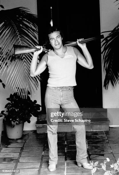 Portrait of British musician and lyricist Bernie Taupin as he poses with a shotgun over his shoulders, Los Angeles, California, April 1980.