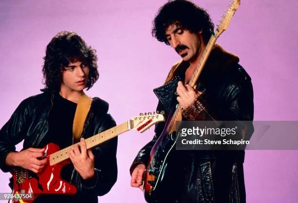 American musicians Dweezil Zappa and his father, Frank Zappa , both in leather coats and with guitars, as they pose in front of a violet background,...