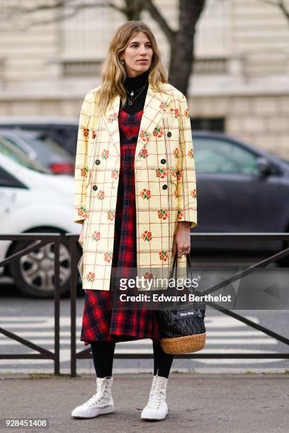 Veronika Heilbrunner wears a flower print checked coat, a red checked pattern dress, a bag, white shoes, outside Miu Miu, during Paris Fashion Week...