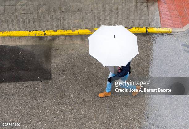 high angle view of person with umbrella walking in the rain on street with white umbrella and with a baby in the rucksack .valencia, spain - wet jeans stock-fotos und bilder